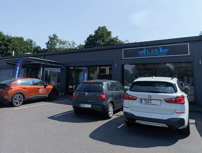 Außenansicht L&S Bauelemente, Showroom mit geparkten Autos am Eingang.